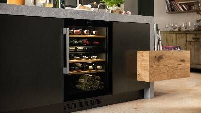 Cucina moderna con cantinetta da incasso e bottiglie visibili, accanto a un cassetto in legno