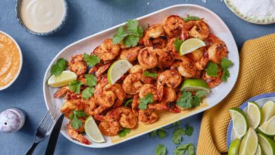 Gegrillte Garnelen mit Limettenspalten obendrauf liegen auf einem blauen Teller, der von Geschirr umgeben ist.