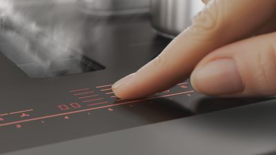 Persoon gebruikt de Uitgebreide Braadsensor op de matzwarte kookplaat terwijl de geïntegreerde ventilatie effectief stoom afzuigt