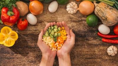 Vista dall'alto di mani che sostengono verdura tagliata a cubetti sopra un tavolo di legno con altre verdure intorno