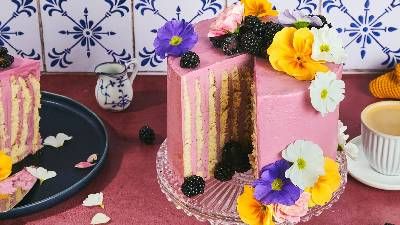 Una torta rosa splendidamente stratificata adornata con fiori vivaci e more, servita con caffè su un tavolo rustico.