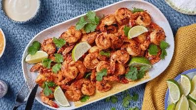 Un piatto di gamberi grigliati guarnito con spicchi di lime e coriandolo fresco, circondato da varie salse e tovaglioli colorati.