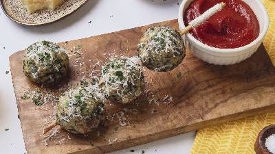 Quattro palline salate di erbe e formaggio su una tavola di legno, guarnite con formaggio grattugiato, servite con una ciotola di salsa marinara.