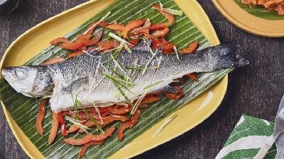 Pesce intero alla griglia guarnito con cipolle verdi e peperoni rossi su una foglia di banana, servito su un piatto giallo.