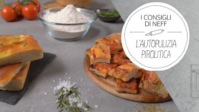 Focaccia e pizza appena sfornate su un piano da cucina, con ingredienti sullo sfondo