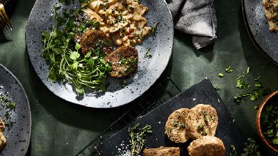 Quattro piatti di pasta, carne ed erbe su tavolo verde. 