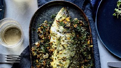 Pesce arrosto con erbe e verdure su piatto scuro. 