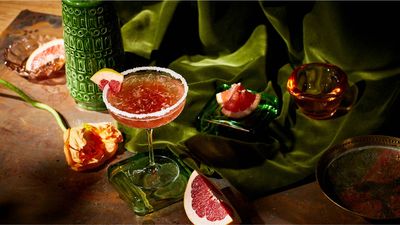 Three stylish cocktails on a decorative tray, surrounded by limes, bottles, fruit, and herbs, exuding a festive atmosphere.