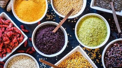 Ciotole con superfood in polvere e semi assortiti disposte su tavolo scuro