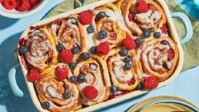 Ovenschaal met versgebakken kaneelbroodjes, overgoten met glazuur en gegarneerd met verse frambozen en bosbessen.   