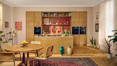 Cucina moderna con mobili in legno, un'isola centrale, tavolo da pranzo con sedie, piante da interno e un tappeto con motivi colorati.