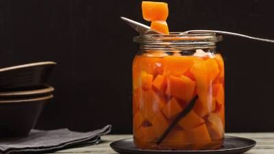 Barattolo di vetro con cubetti di zucca appoggiato su un piatto nero e cucchiaio che ne solleva un pezzo