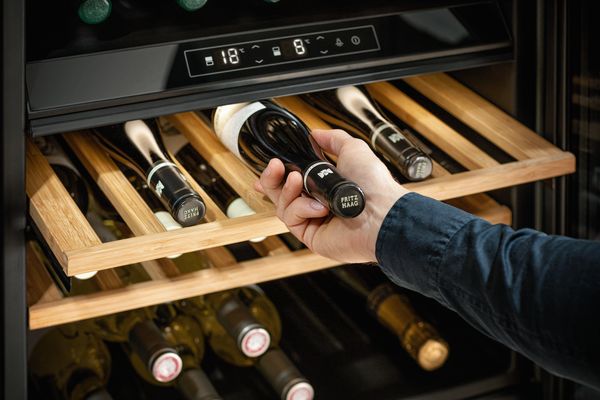 Uomo che ripone una bottiglia di vino sul ripiano della cantinetta NEFF 