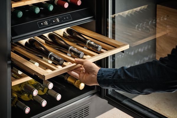 Uomo che estrae un ripiano scorrevole della cantinetta vino da incasso NEFF per visionare le bottiglie