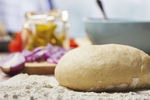 Impasto lievitato su piano infarinato con ingredienti sullo sfondo