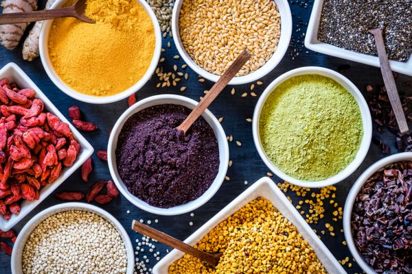 Ciotole con superfood in polvere e semi assortiti disposte su tavolo scuro