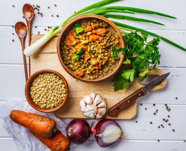 Zuppa di lenticchie con carote e prezzemolo in ciotola di legno, con ingredienti freschi su tagliere