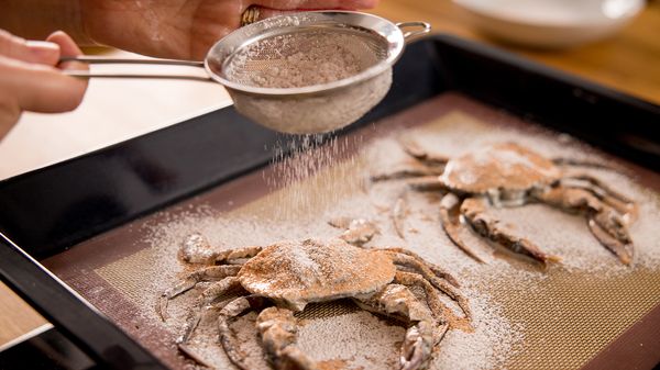 Person sprinkling mix over crabs in baking tray