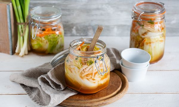 Barattoli con cavolo e carote fermentate su tavolo chiaro, con tovagliolo, cucchiaio di legno e tazze accanto