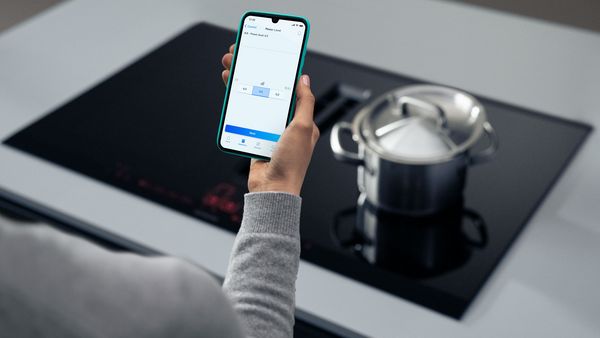 Personne utilisant un smartphone sur le plateau &agrave; induction avec tasse &agrave; caf&eacute; en arri&egrave;re-plan.