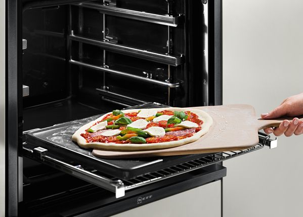 Mano che inforna una pizza Margherita, posizionandola sulla pietra refrattaria