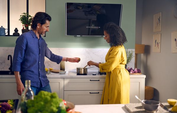 Giovane coppia che cucina con piano cottura a induzione e cappa a parete Neff