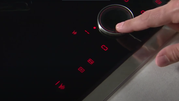 Mano regola la manopola su un piano cottura moderno, con pulsanti rossi che indicano i livelli di calore. 