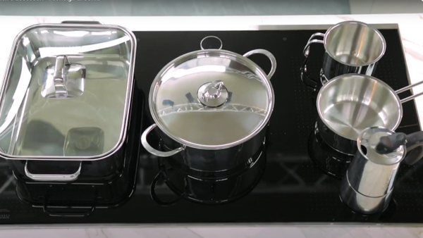 Piano di cucina moderno con diversi utensili in acciaio inox, tra cui pentola con coperchio, tazze e teglia. 