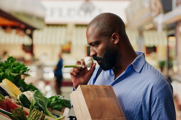 Uomo al bancone degli ortaggi che annusa una testa d’aglio