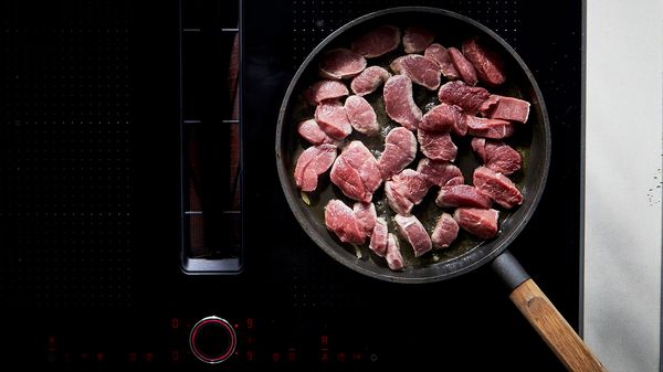 A pan on the hob, filled with sliced lamb fillet.