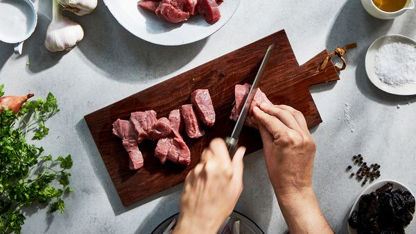 A person cutting fresh lamb fillet on a board.