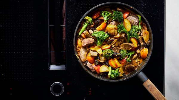 A pan on the hob, filled with fried lamb fillet and vegetables.
