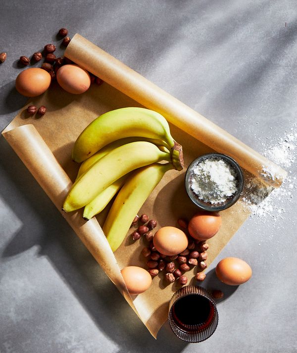 Fresh bananas, some eggs, nuts and sugar in a little bowl on parchment paper.