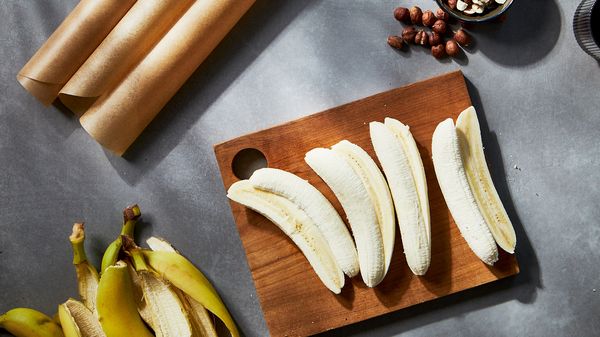 Bananas, sliced into hald on a wooden board beneath their peel and somt nuts in a small bowl.