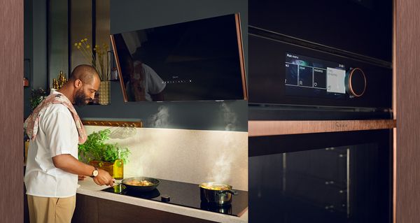 Chris Glass, gedraaid naar een dampende pan op de kookplaat, close-up van afwerkingsstrips in Brushed Bronze op de oven 
