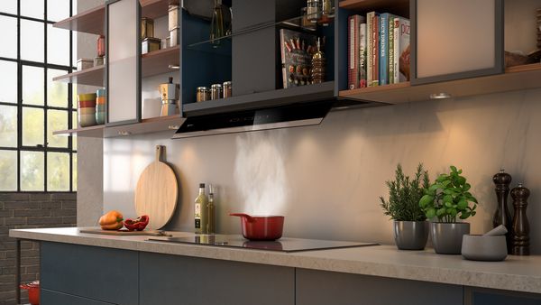Eine in Küchenmöbel integrierte Dunstabzugshaube, Dampf steigt aus einem roten Topf aus  