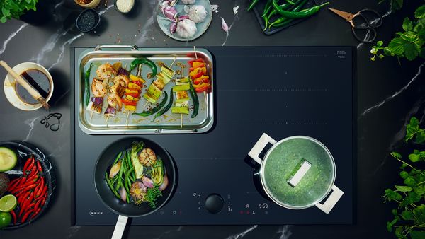 Légifelvétel a főzőlapról, edényről, serpenyőről és grillserpenyőről, amely egy kibővített főzőzónát mutat  