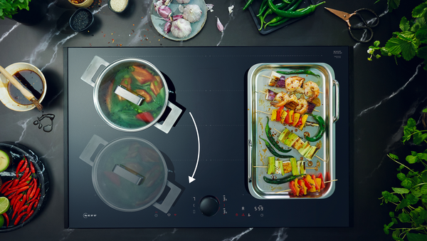 Vista dall'alto di un piano cottura moderno con una pentola con verdure e una teglia di gamberetti grigliati con tanti spiedini colorati e altri ingredienti freschi.
