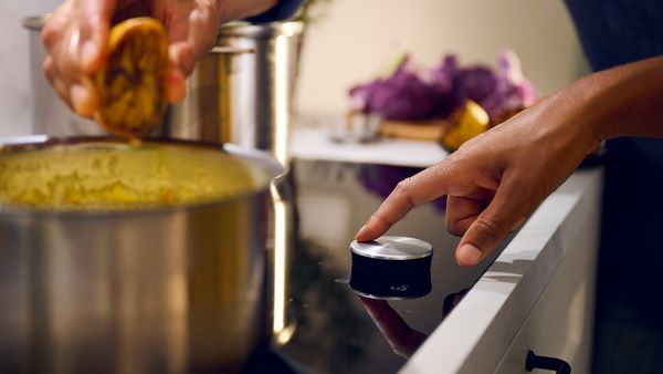Egy kéz használja a Twist Pad tárcsát a főzőlapon, háttérben lila zöldségekkel, előtérben kifacsart citrommal 