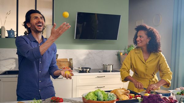 Man throwing lemon, woman laughing in front of inclined hood mounted on green wall 
