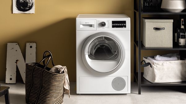 A free-standing tumble dryer with a bag of clothes beside an open shelving unit