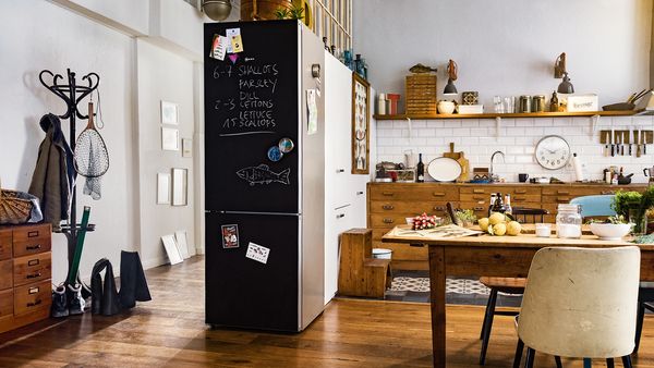 Világos konyha, szabadon álló kombinált hűtőkészülékkel matt fekete üvegből, rajta kréta felirat és képeslapok