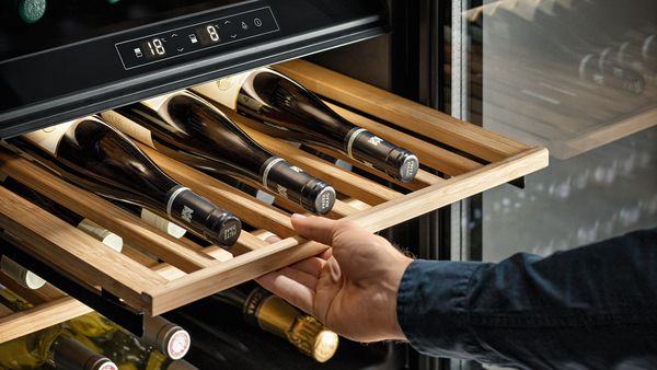 A hand sliding out a shelf from a wine cooler