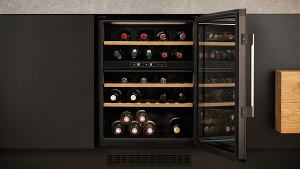An open wine cooler with multiple bottles inside, underneath a kitchen island