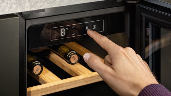 Une main changeant les paramètres du panneau électronique situé au sommet d'une cave à vin ouverte.