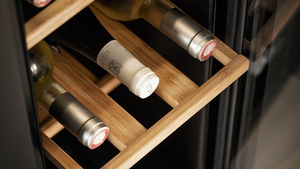 Een close-up van een bamboe plateau in een open wijnklimaatkast met drie wijnflessen erop