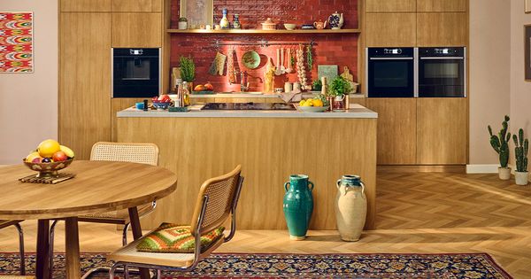 Cucina con isola centrale in legno, parete in mattoni decorata con utensili, elettrodomestici integrati e tavolo rotondo