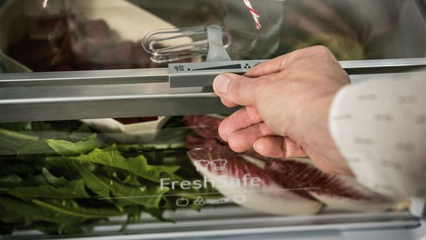 A hand adjusting the Eco Air Flow system above a Fresh Safe drawer inside a fridge