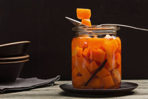 Barattolo di vetro con cubetti di zucca appoggiato su un piatto nero e cucchiaio che ne solleva un pezzo