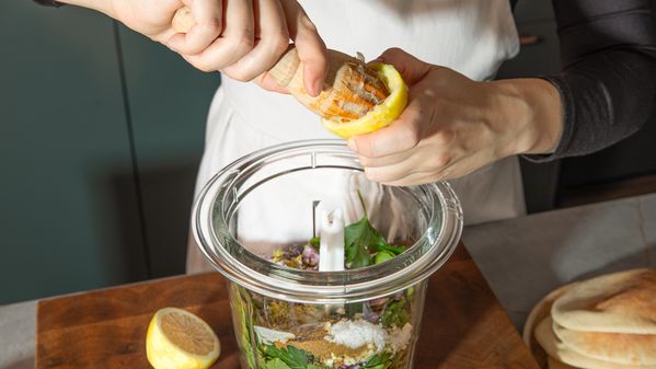 Adding the zest of half a lemon in a food processor filled with ingredients 